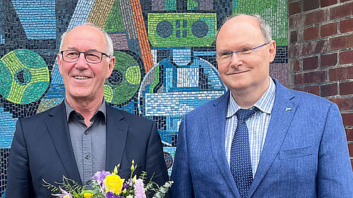 Die beiden Personen stehen nebeneinander auf dem Campus. Prof. Rachow hält einen Blumenstrauß in der Hand.