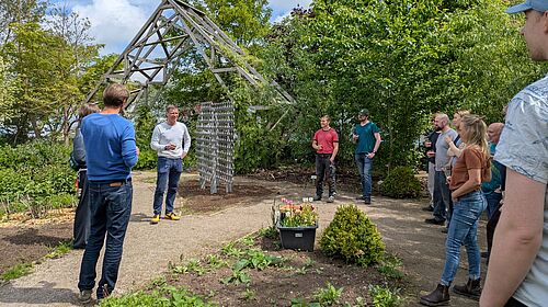 Hochschulangehörige stehen in einem Garten im Kreis um Prof. Hillmann herum, der eine Rede hält.